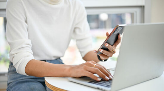 an Asian woman using her smartphone and laptop, remote working at the coffee shop.